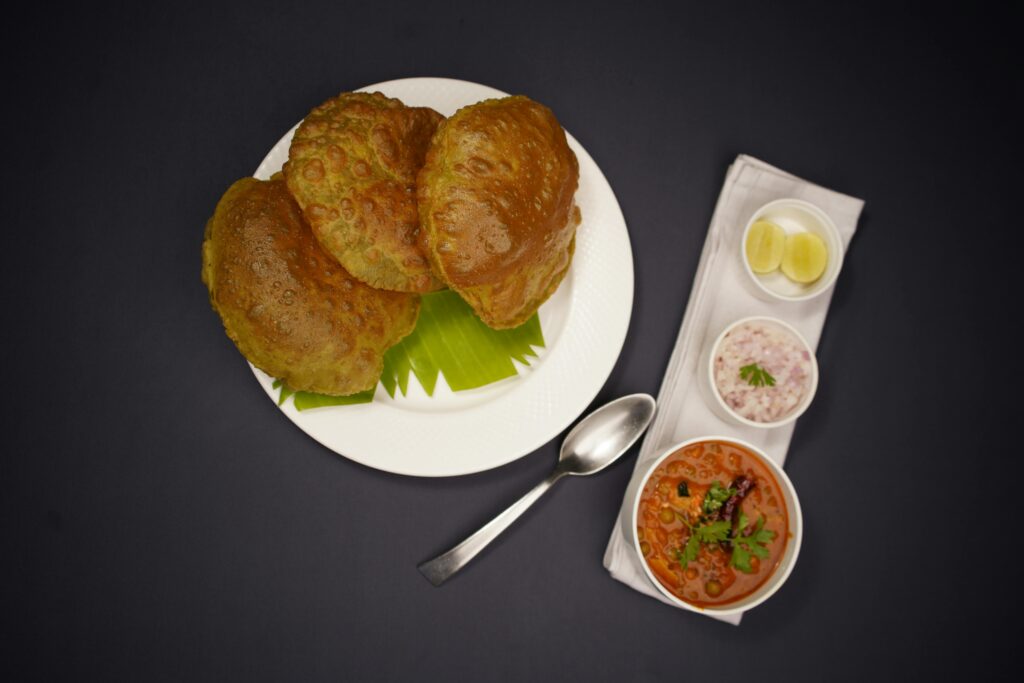 Top view of puri with curry and sides, featuring vibrant colors and textures on a dark background.