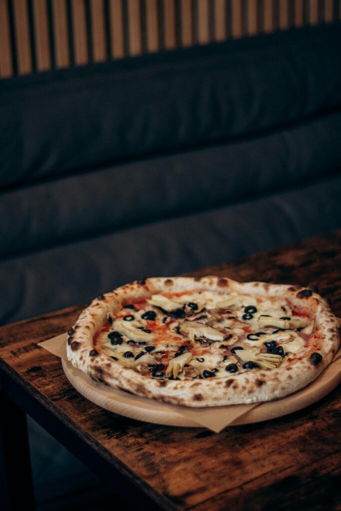 A tantalizing vegetarian pizza topped with fresh olives and mushrooms, served on a wooden table.